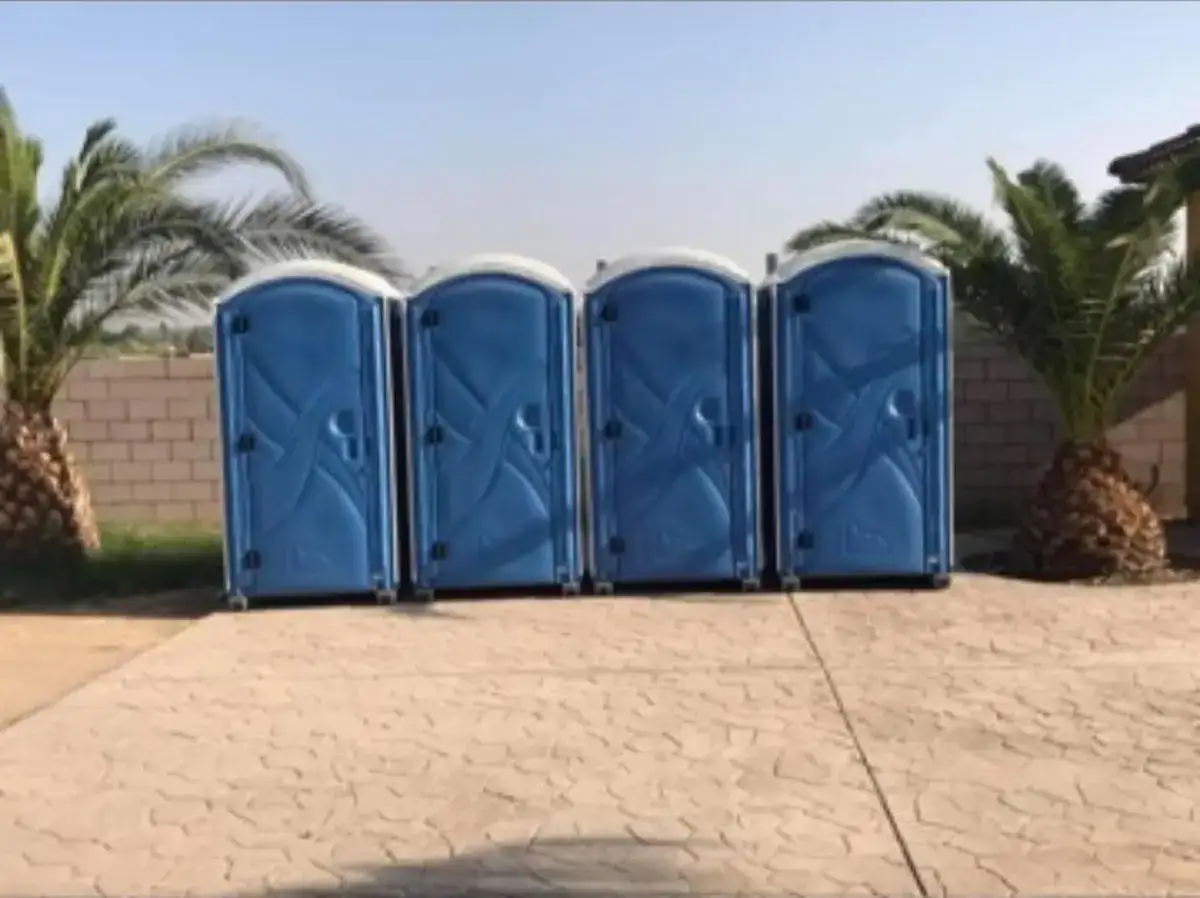 Four portable toilets in a row on a paved lot