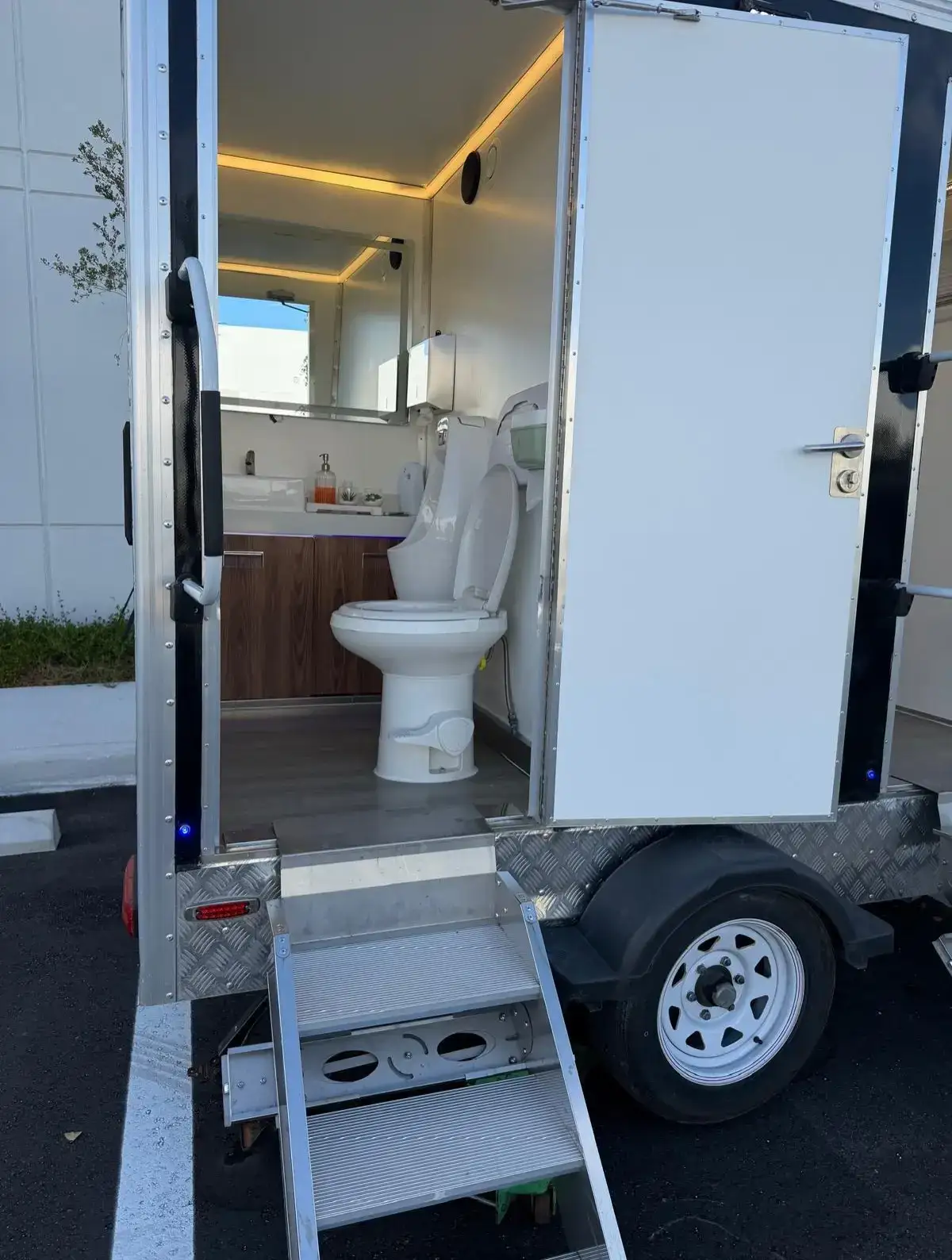 Restroom trailer stall with flush toilet, wood vanity and lit mirror